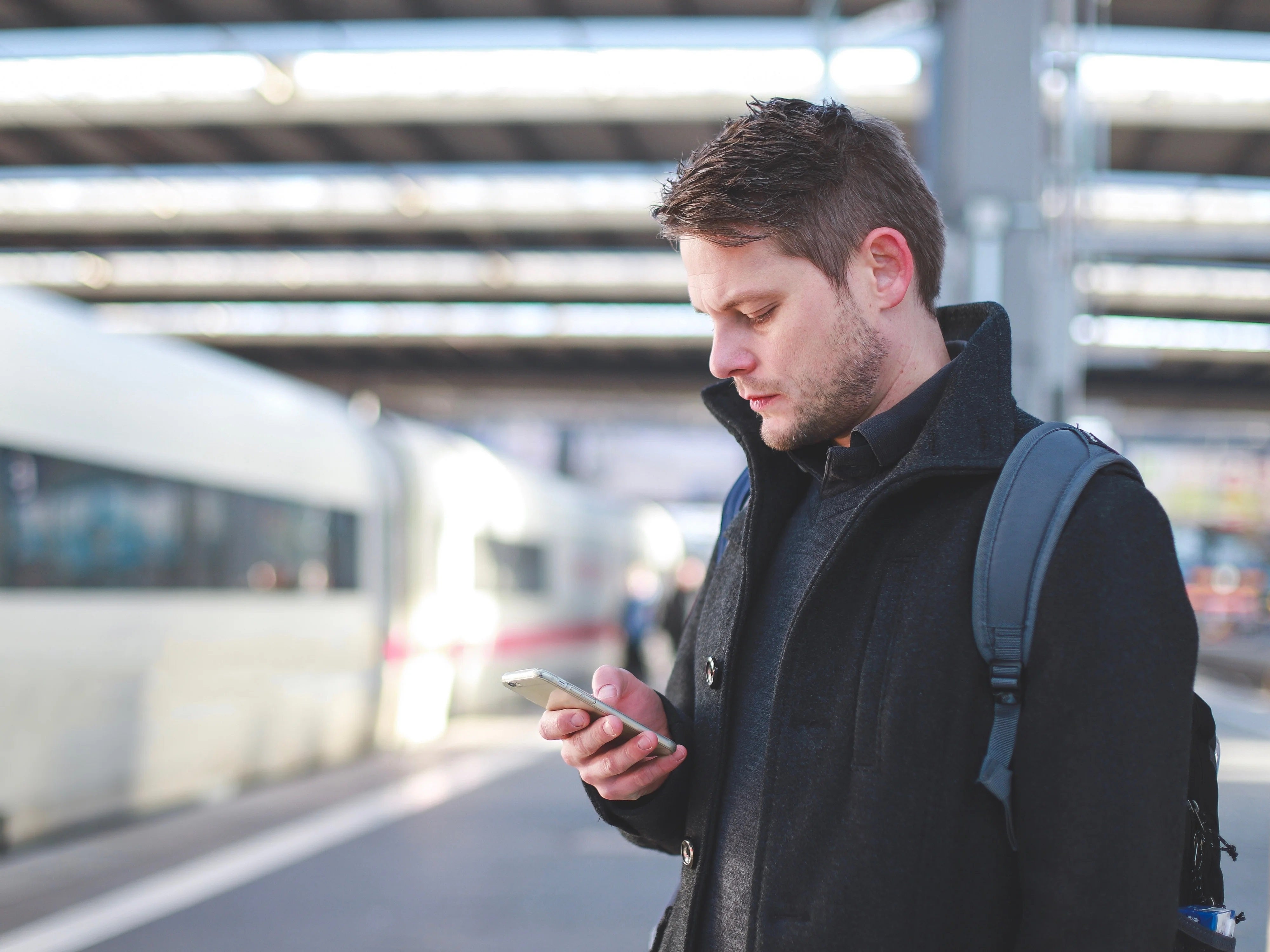 Mann mit Smartphone am Bahnhof vor einem Zug