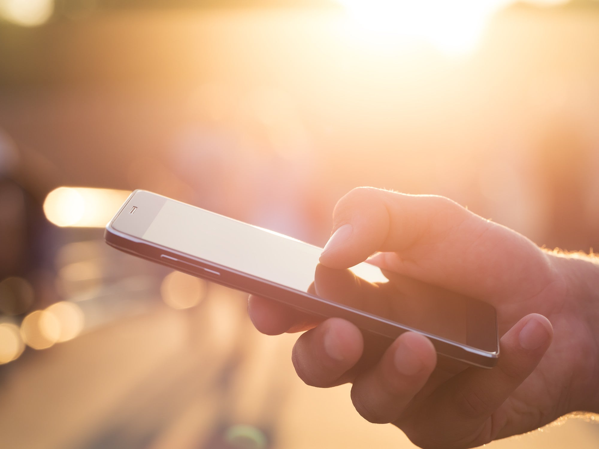 Hand hält ein Handy im Sonnenlicht.