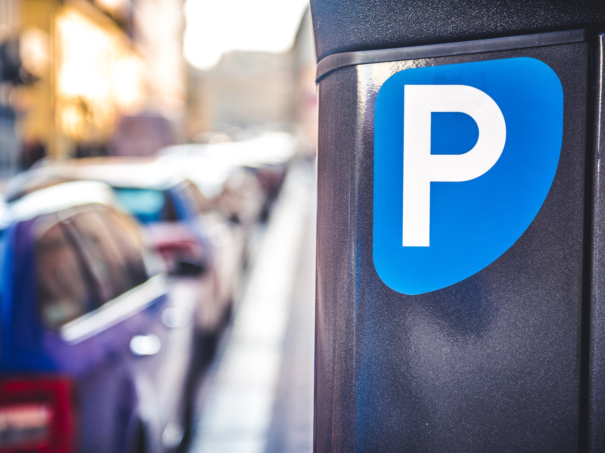 Parkscheinautomat mit Autos im Hintergrund.