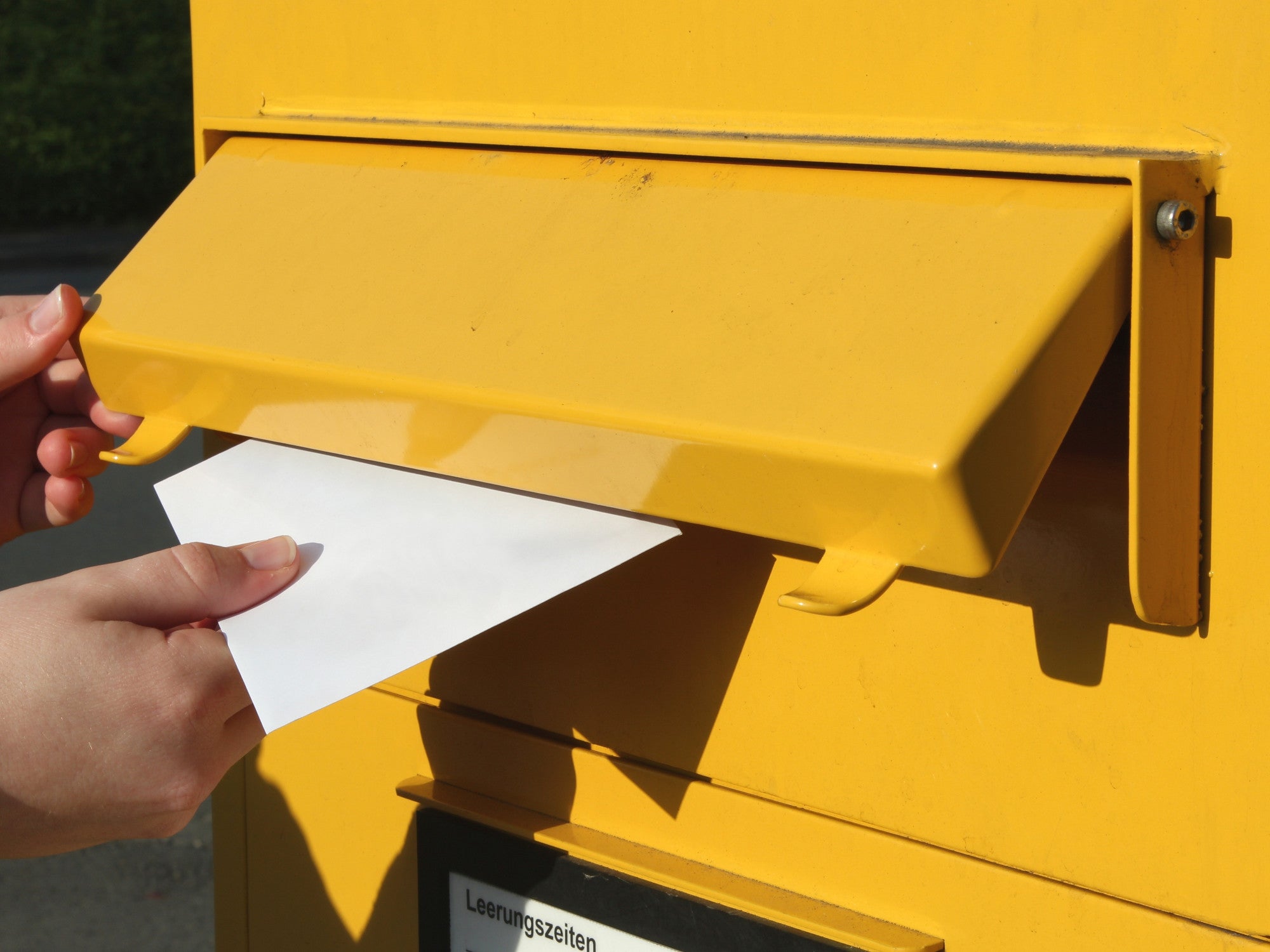 Frau wirft einen Brief in einen Briefkasten ein.