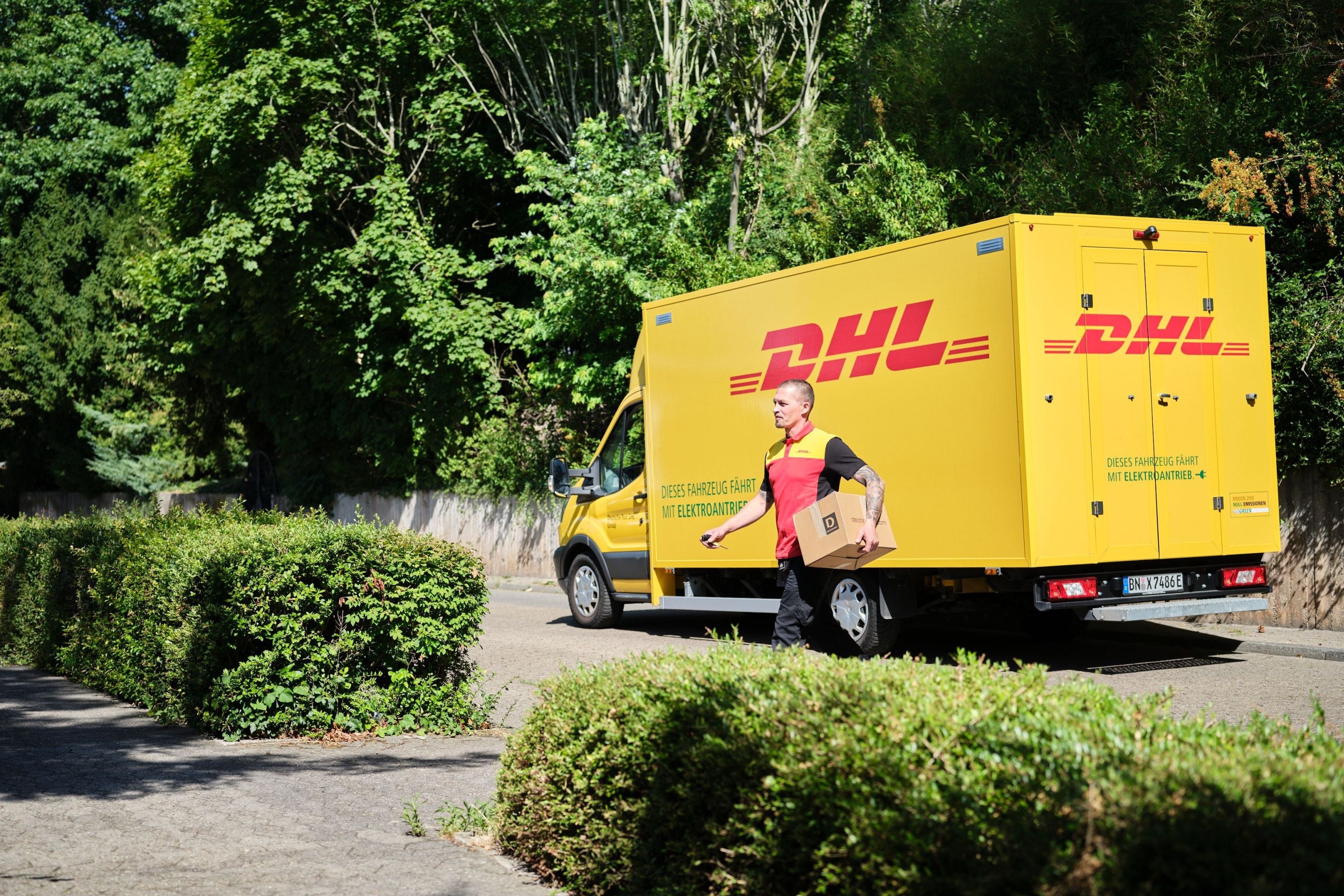 Ein DHL-Zusteller mit einem Paket unter dem Arm verlässt sein Lieferfahrzeug