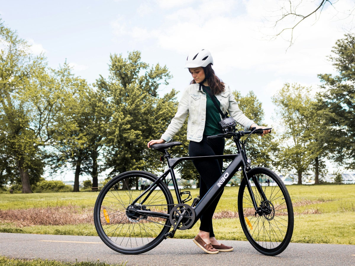 Eine Frau mit Helm hält ein Fahrrad in der Hand und schaut es an.