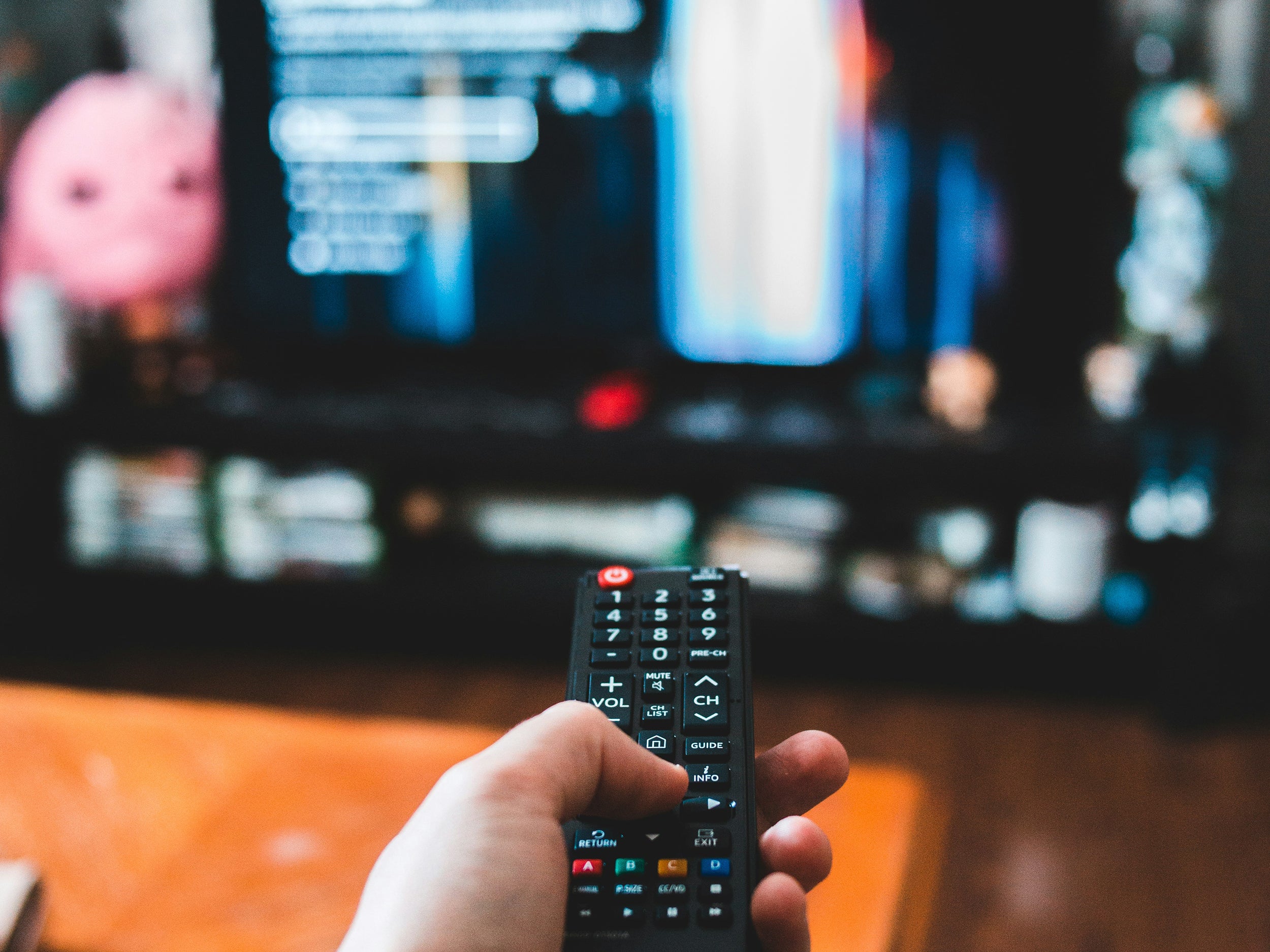 Eine Fernbedienung in einer Hand, die einen Fernseher im Hintergrund steuert