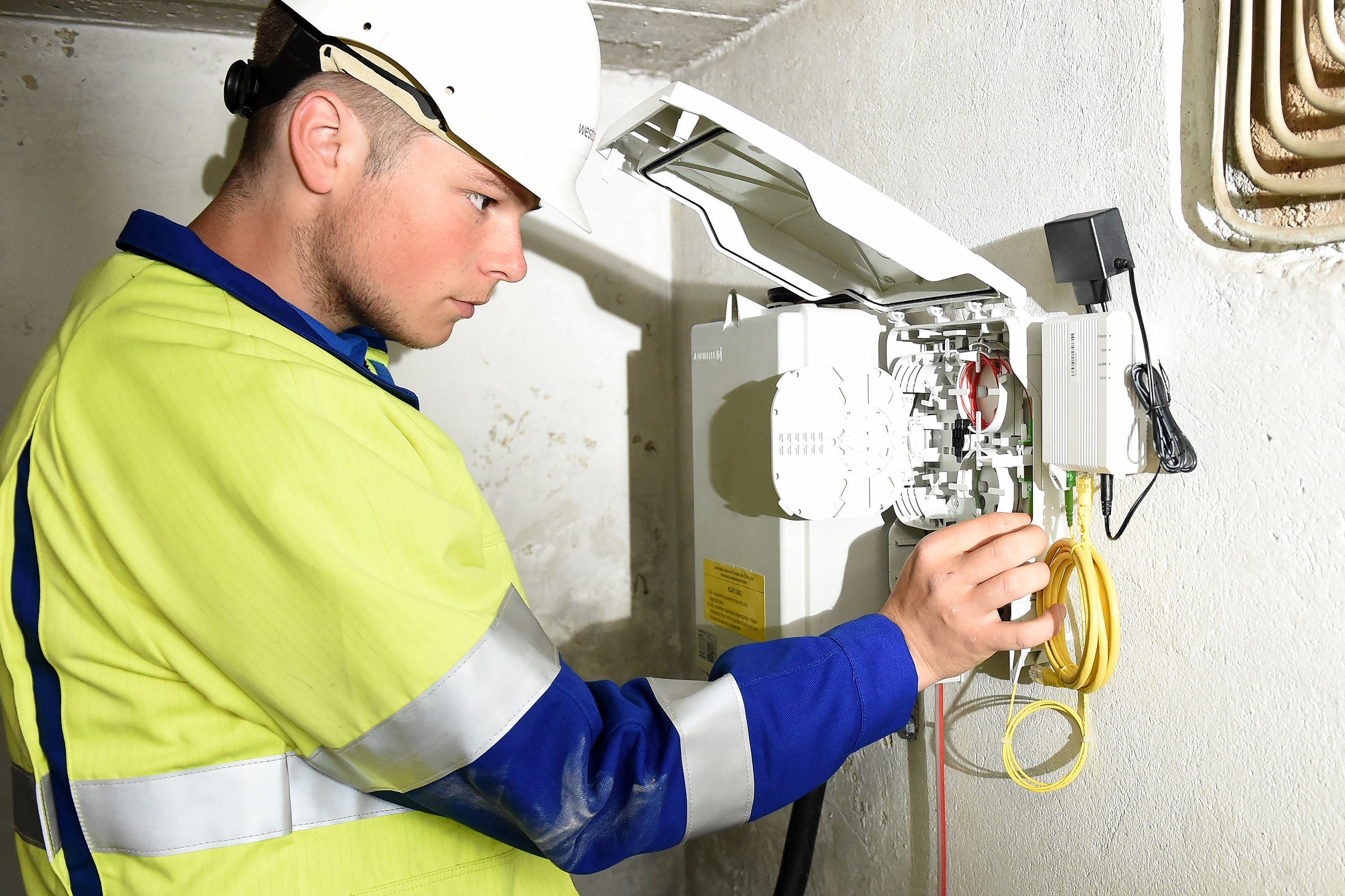 Ein Techniker steht an einem Glasfaseranschluss im Keller eines Hauses