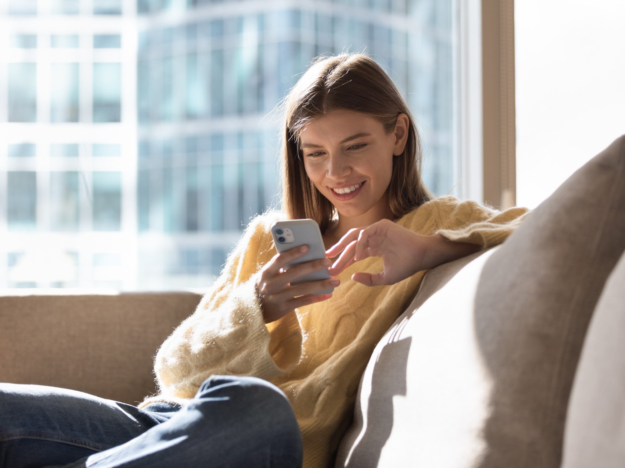 Frau sitzt mit einem Smartphone auf einem Sofa.