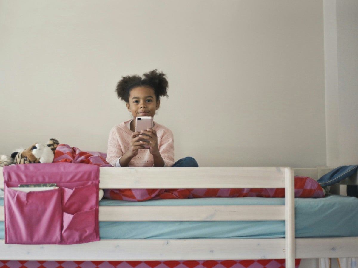 Ein Mädchen sitzt auf einem Bett und hält ein Smartphone in ihrer Hand.