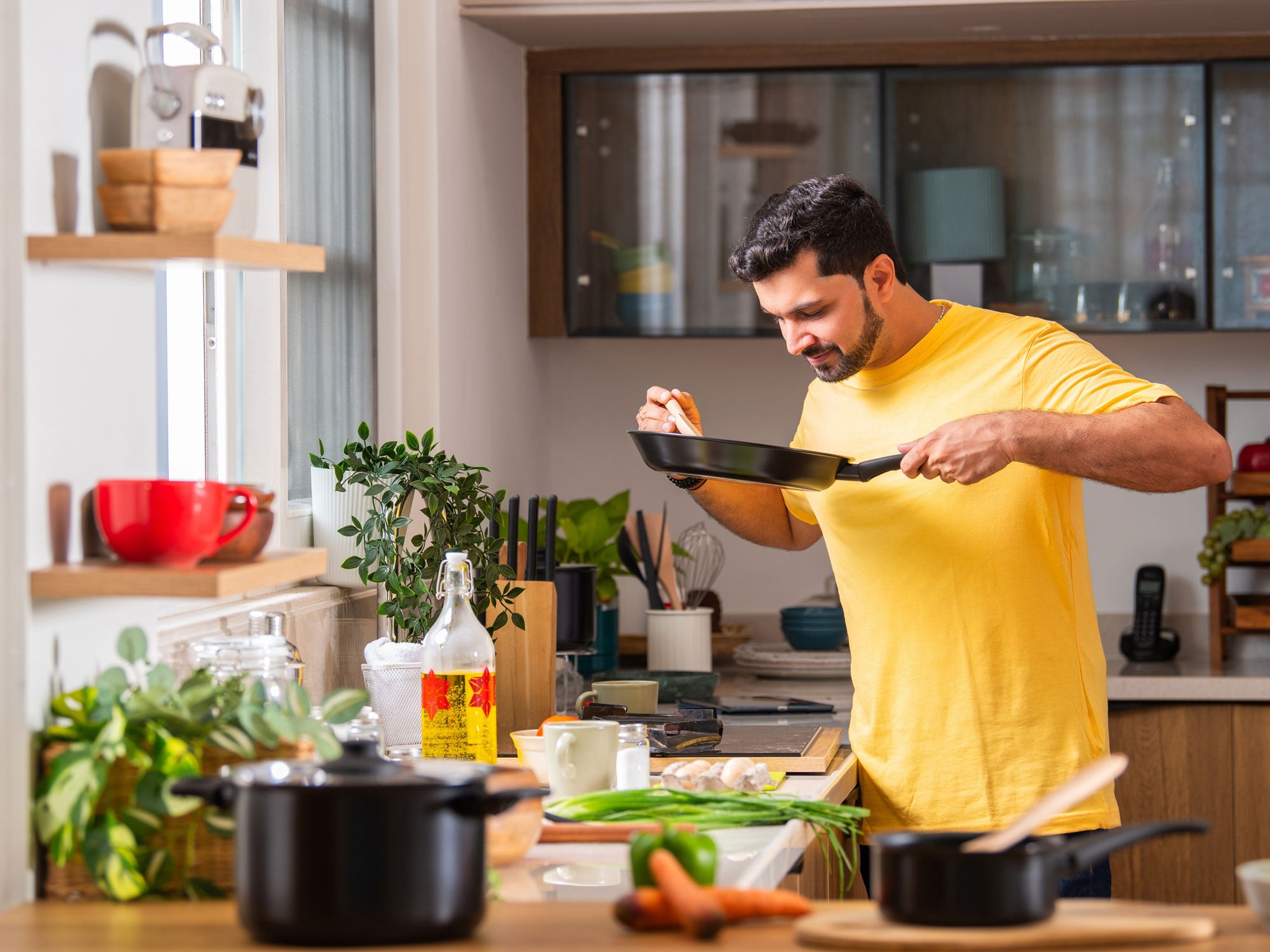 Ein Mann steht in einer Küche und probiert Essen aus einer Pfanne