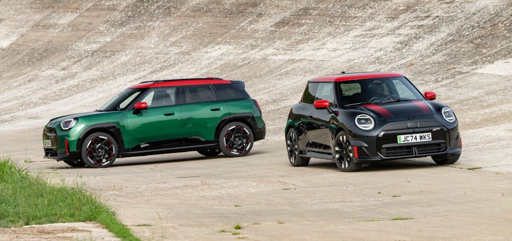 Der MINI John Cooper Works Electric & der MINI John Cooper Works Aceman stehen vor einer Steilwand.