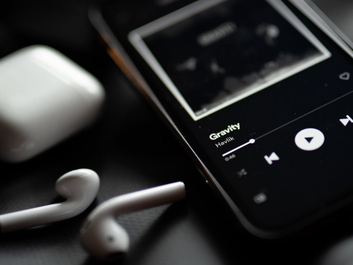 Spotify Premium auf einem Smartphone, daneben kabellose In-Ear-Kopfhörer.