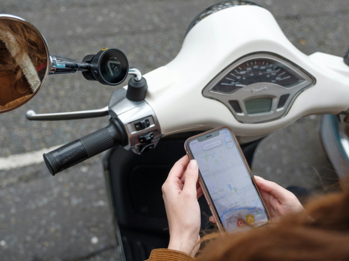 Eine Person hält ein Smartphone mit einer geöffneten Navi-App in der Hand und sitzt auf einem Roller.