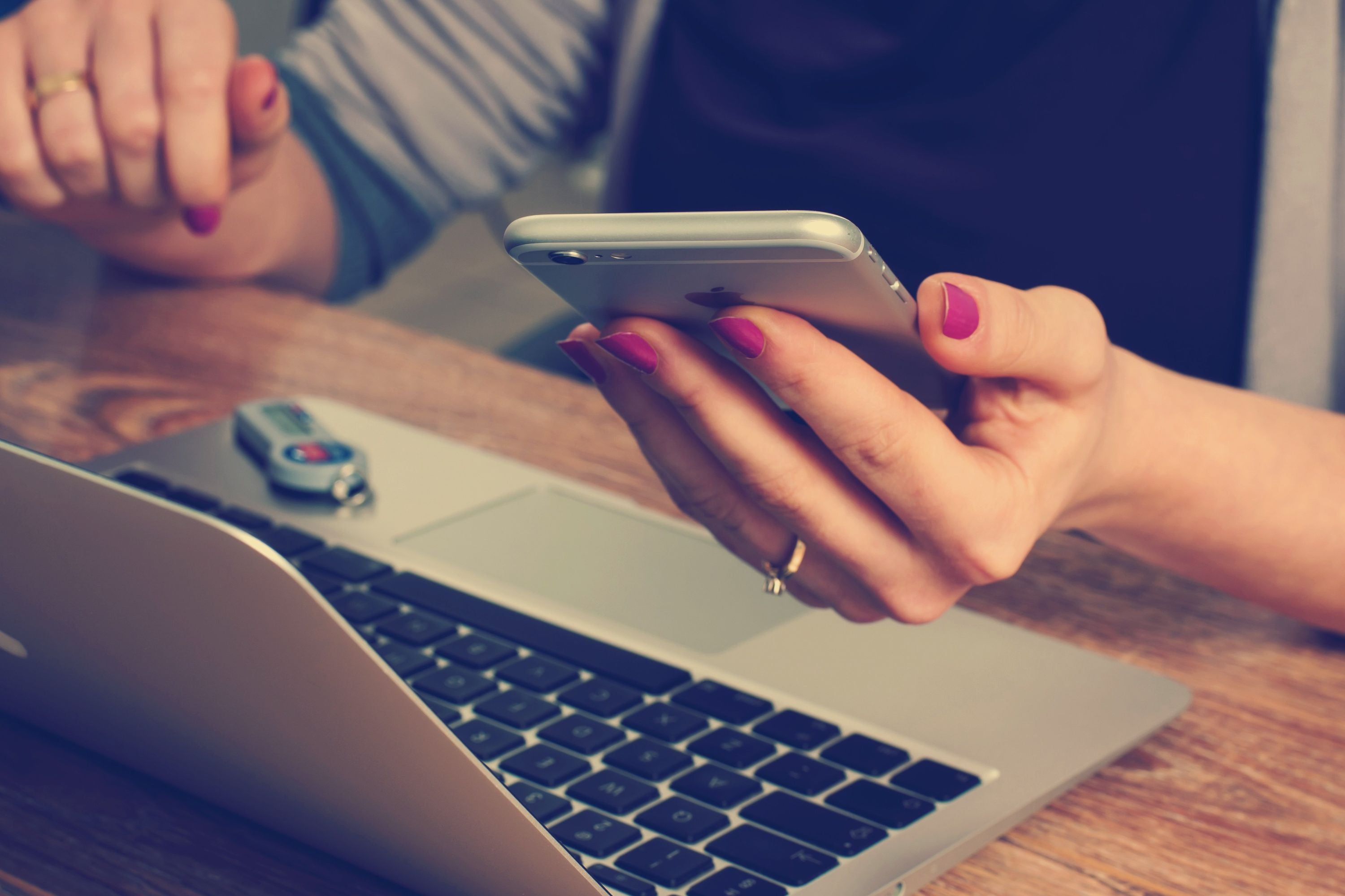 EIn Laptop steht auf einem Tisch, eine Frau hält ein iPhone in der Hand