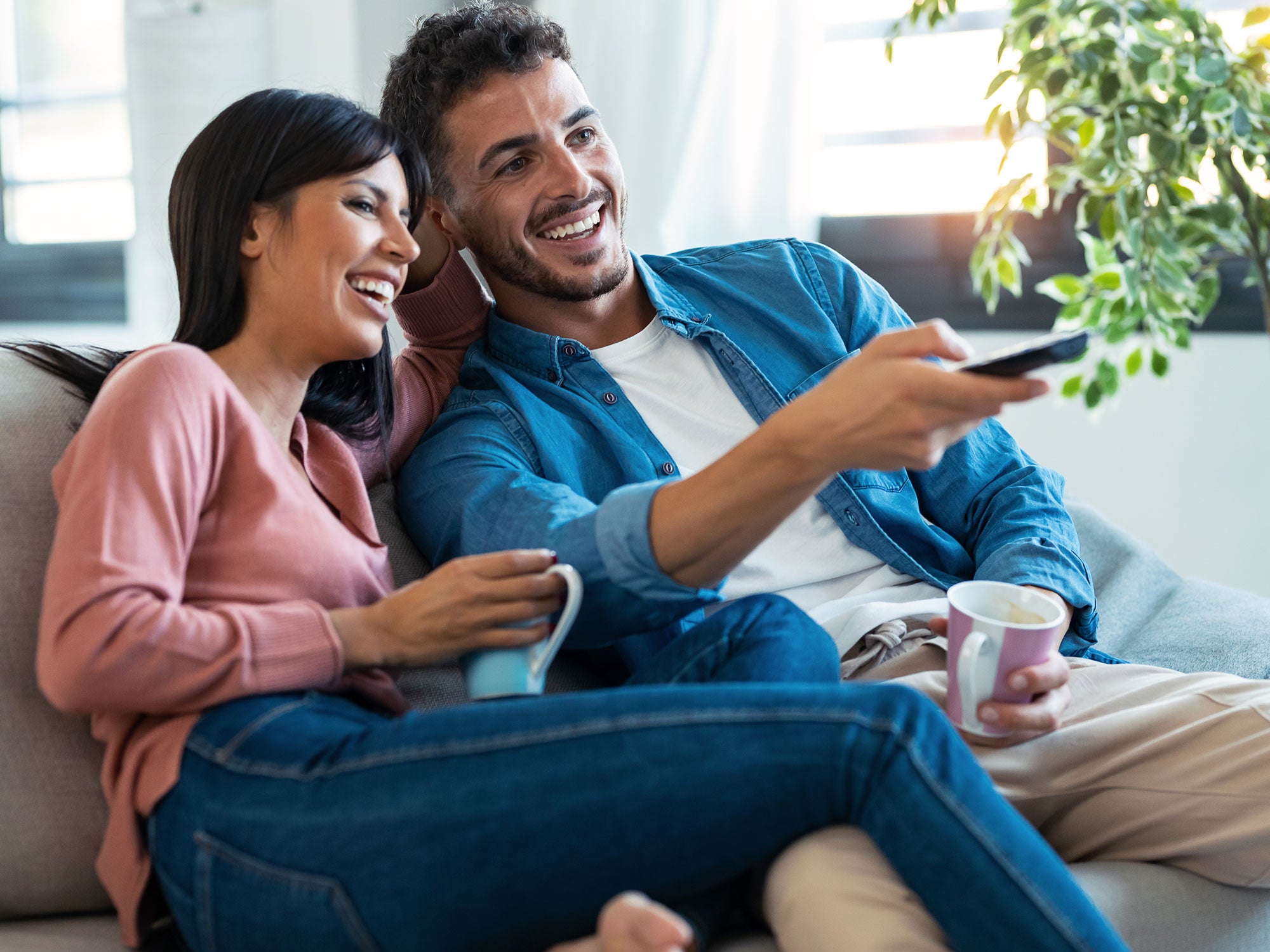 Eine Frau und ein Mann sitzen auf einem Sofa, er bedient eine TV-Fernbedienung