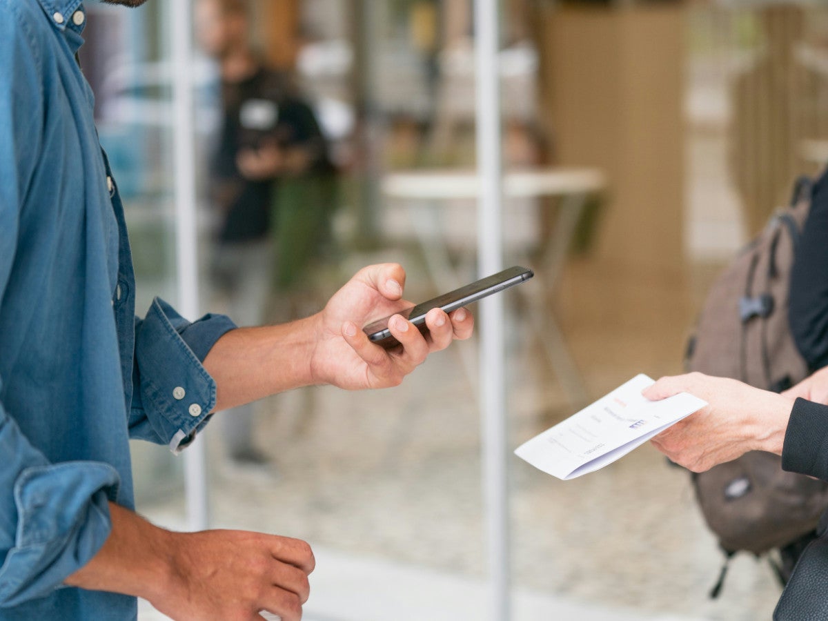 Eine Person scannt mit dem Handy einen QR-Code auf einem Blatt.