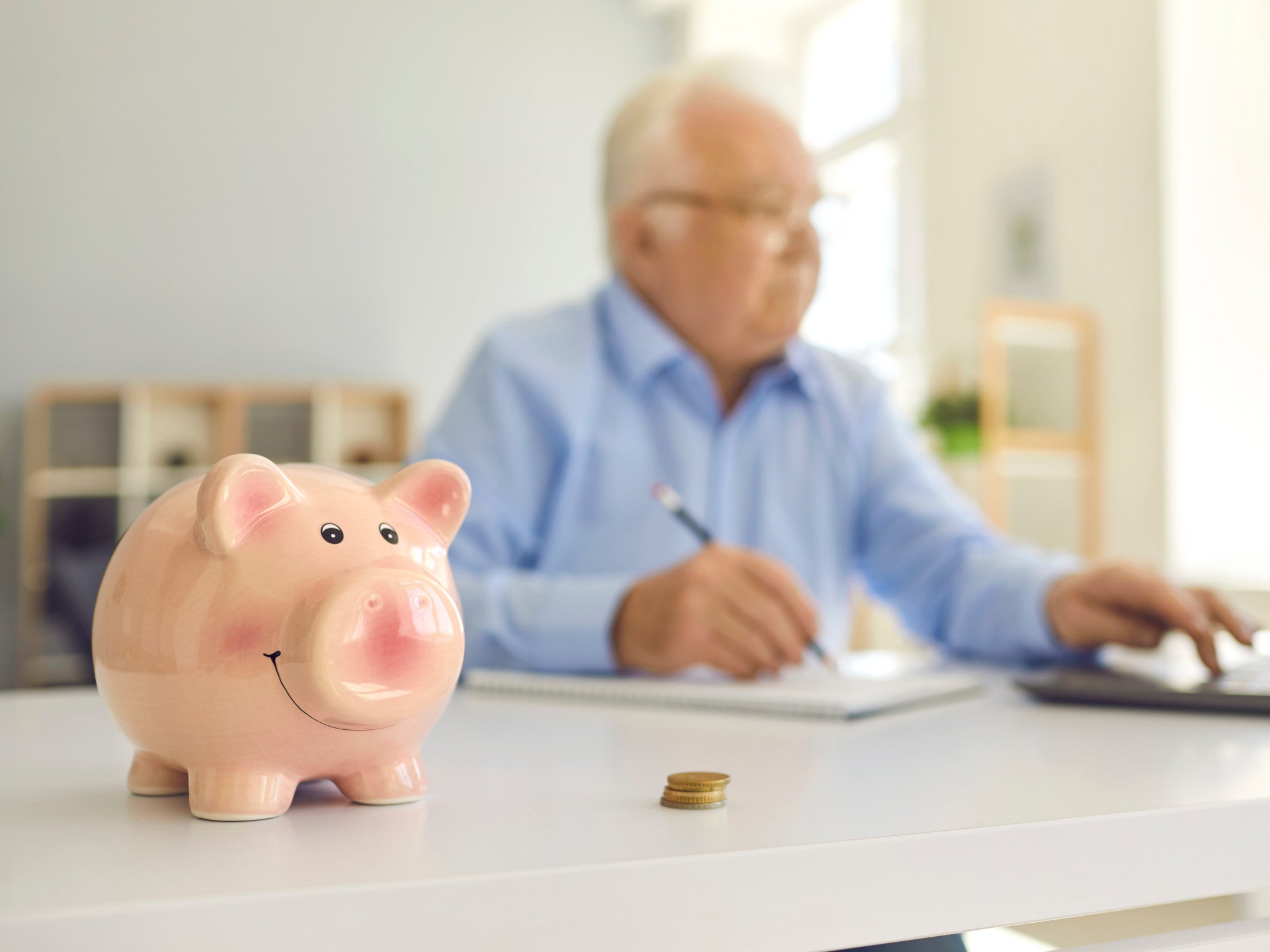 Sparschwein steht neben einem Senior auf dem Schreibtisch.