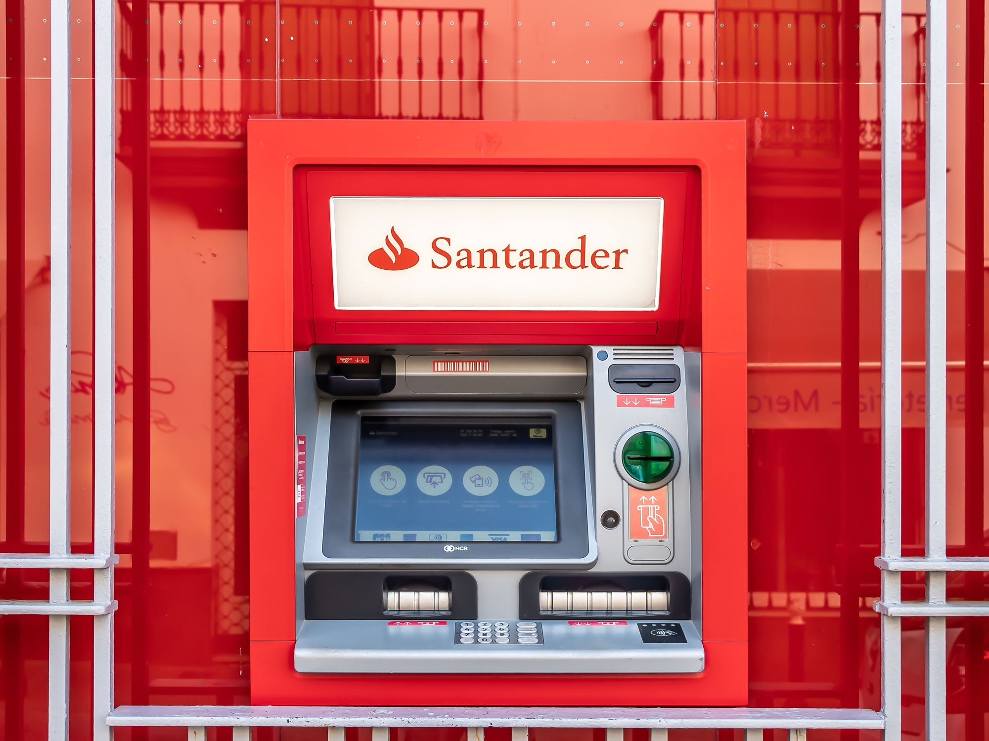 Ein Geldautomat der Santander Bank vor einer roten Glasfront