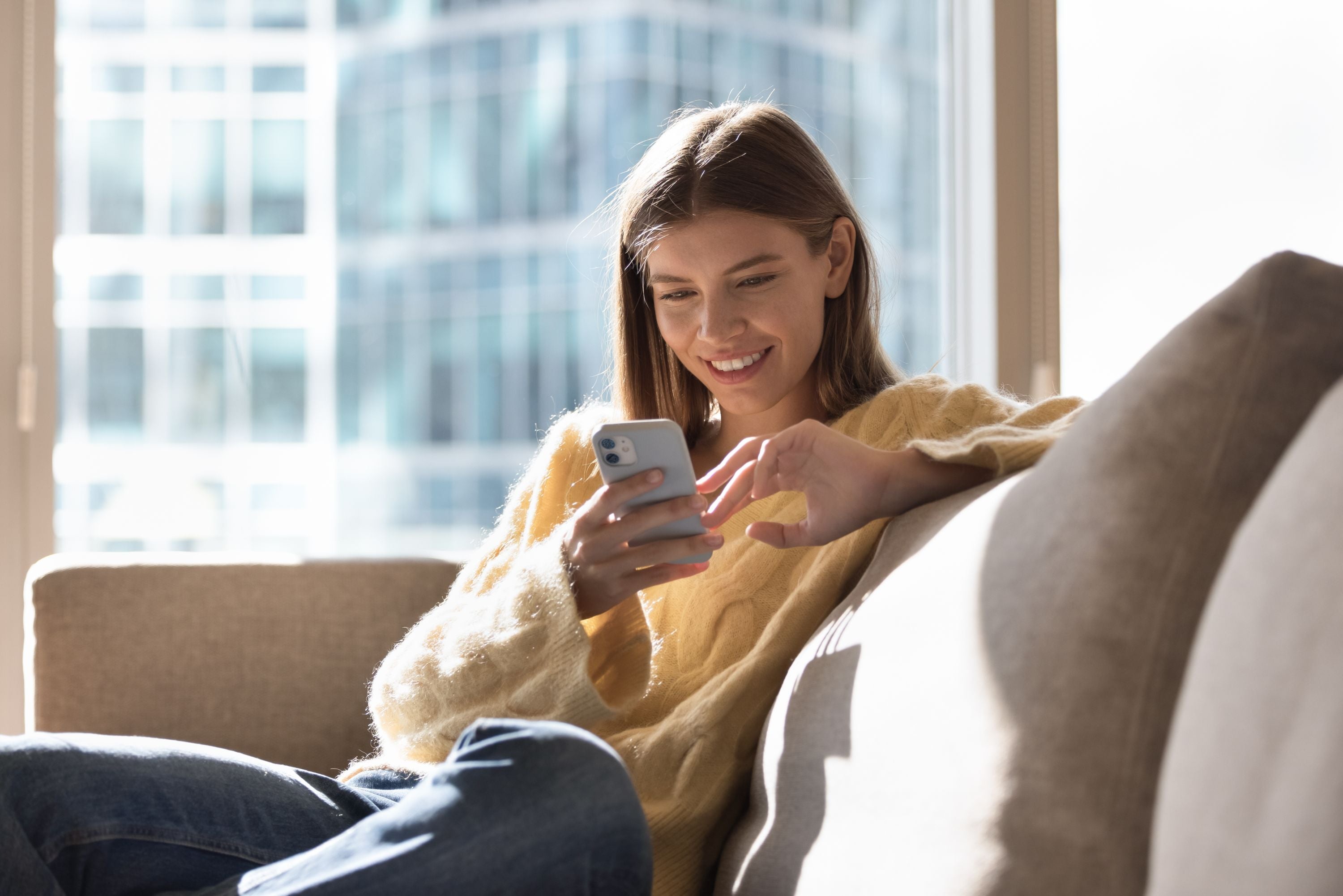 Eine Frau sitzt mit einem Handy auf der Couch