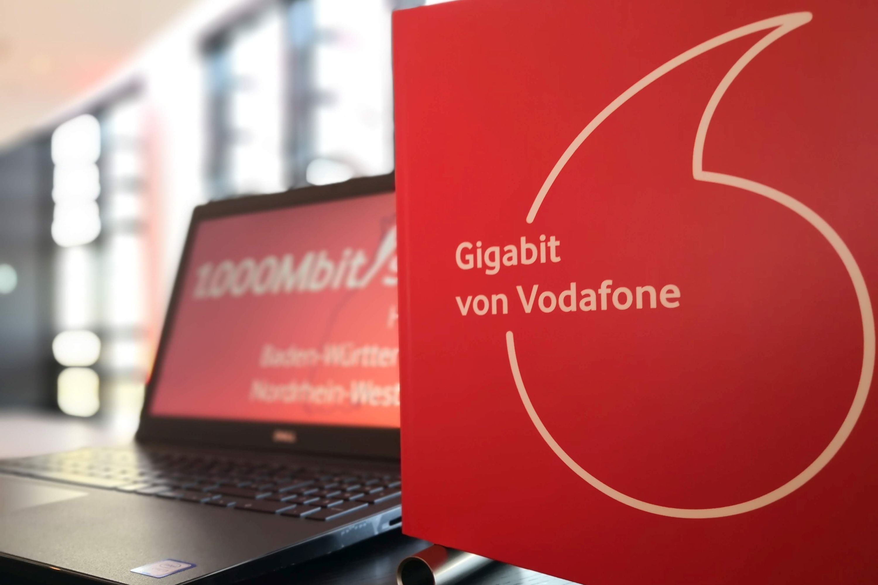 Ein Laptop steht auf einem Tisch, im Vordergrund ein Vodafone-Logo